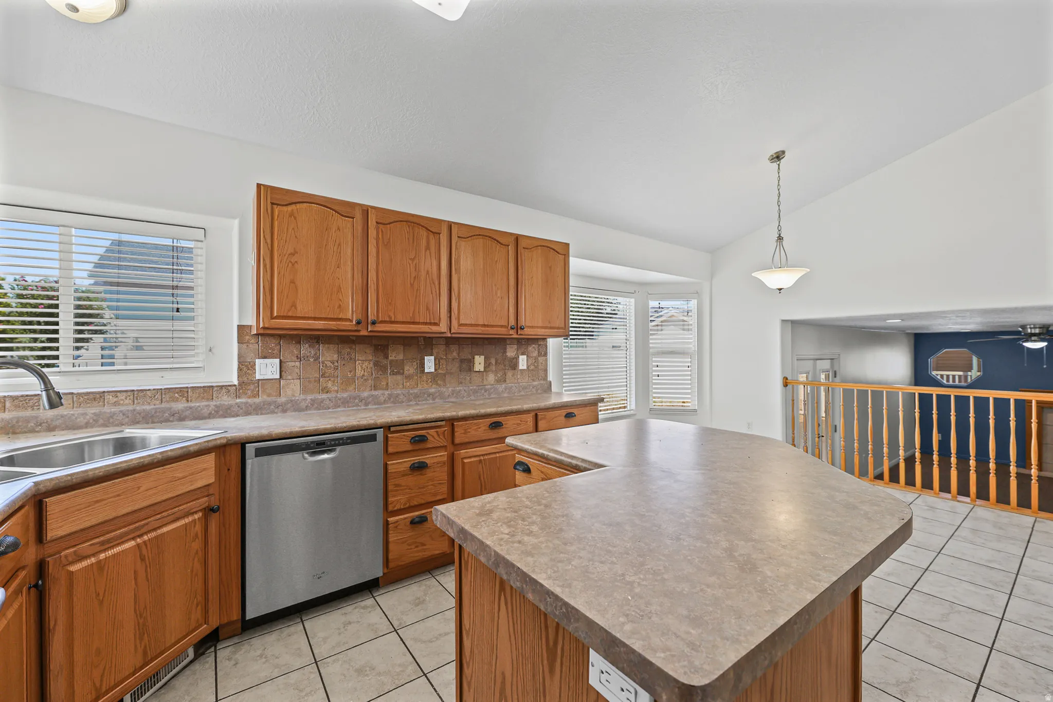Kitchen featuring a U-shaped island with a laminate countertop, light wood cabinetry, stainless steel dishwasher, and a double basin sink