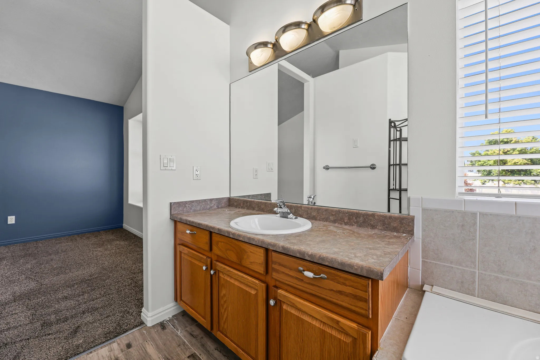 Vanity with wood cabinetry and an integrated sink, featuring a large mirror and three-light fixture