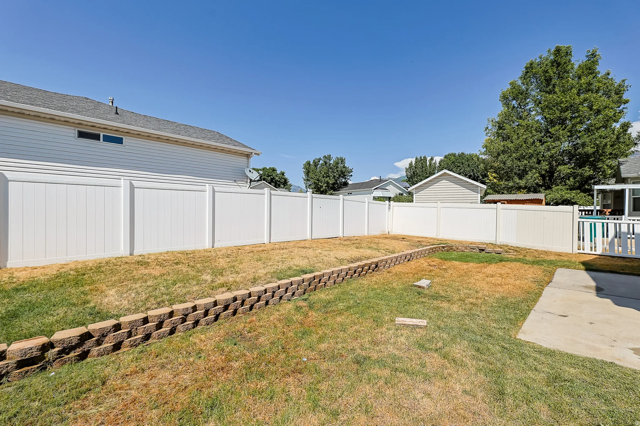 Expansive backyard featuring a white vinyl privacy fence, a concrete patio, and a tiered landscape design with a retaining wall