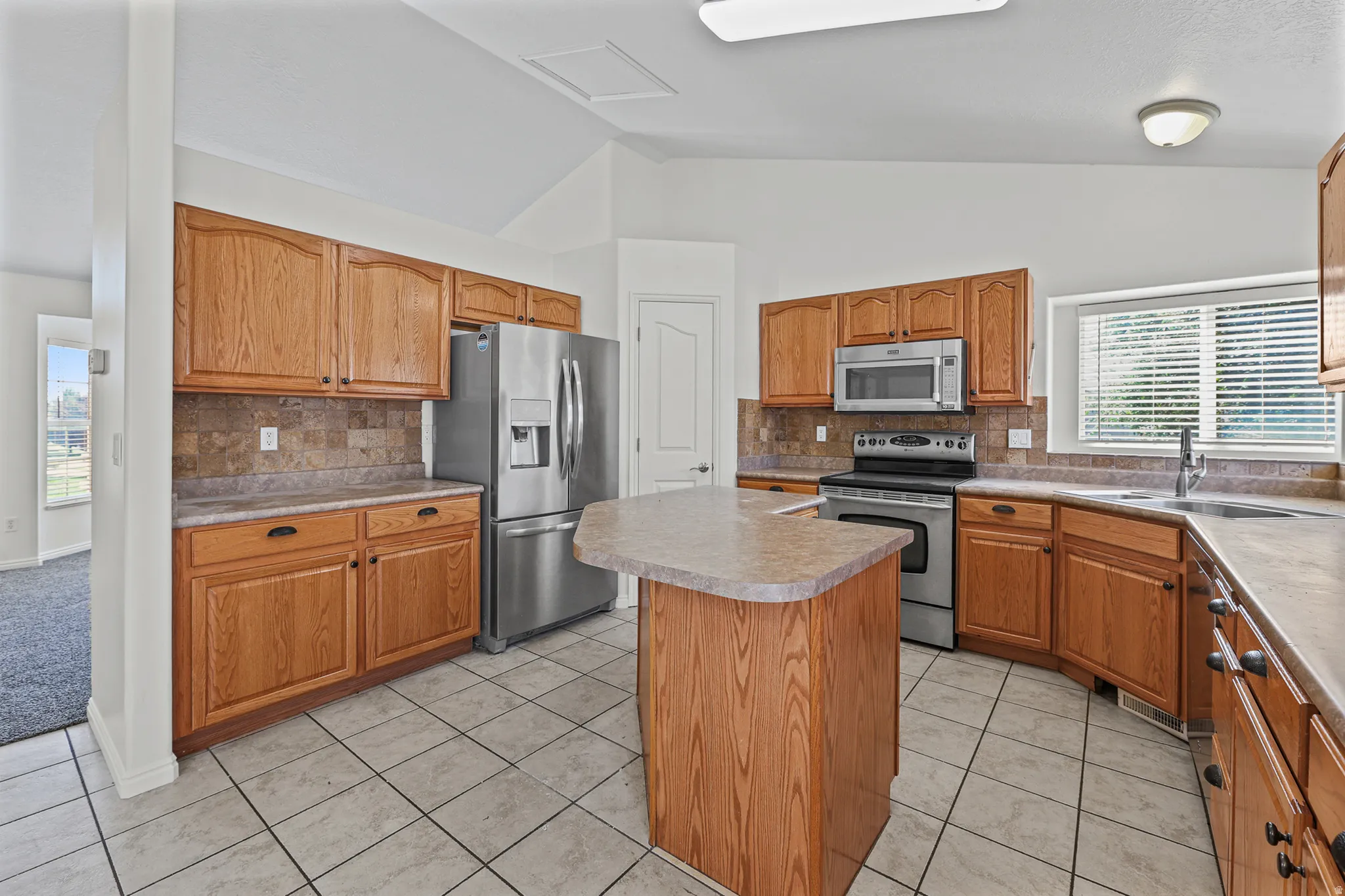 Kitchen featuring a central island, light wood cabinetry, stainless steel appliances, and tile flooring