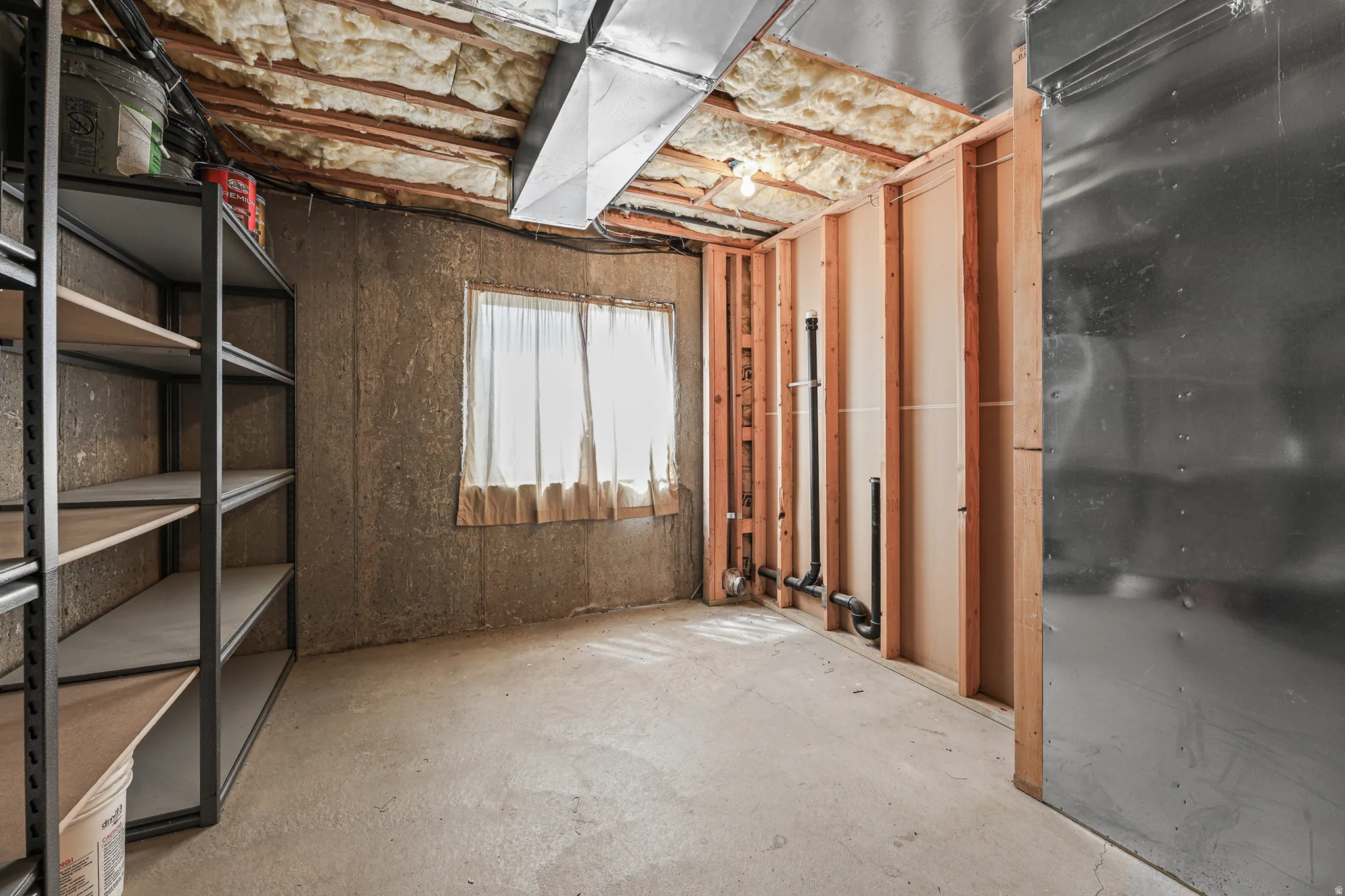 Unfinished basement space featuring exposed ceiling joists with insulation, bare concrete walls, and concrete flooring