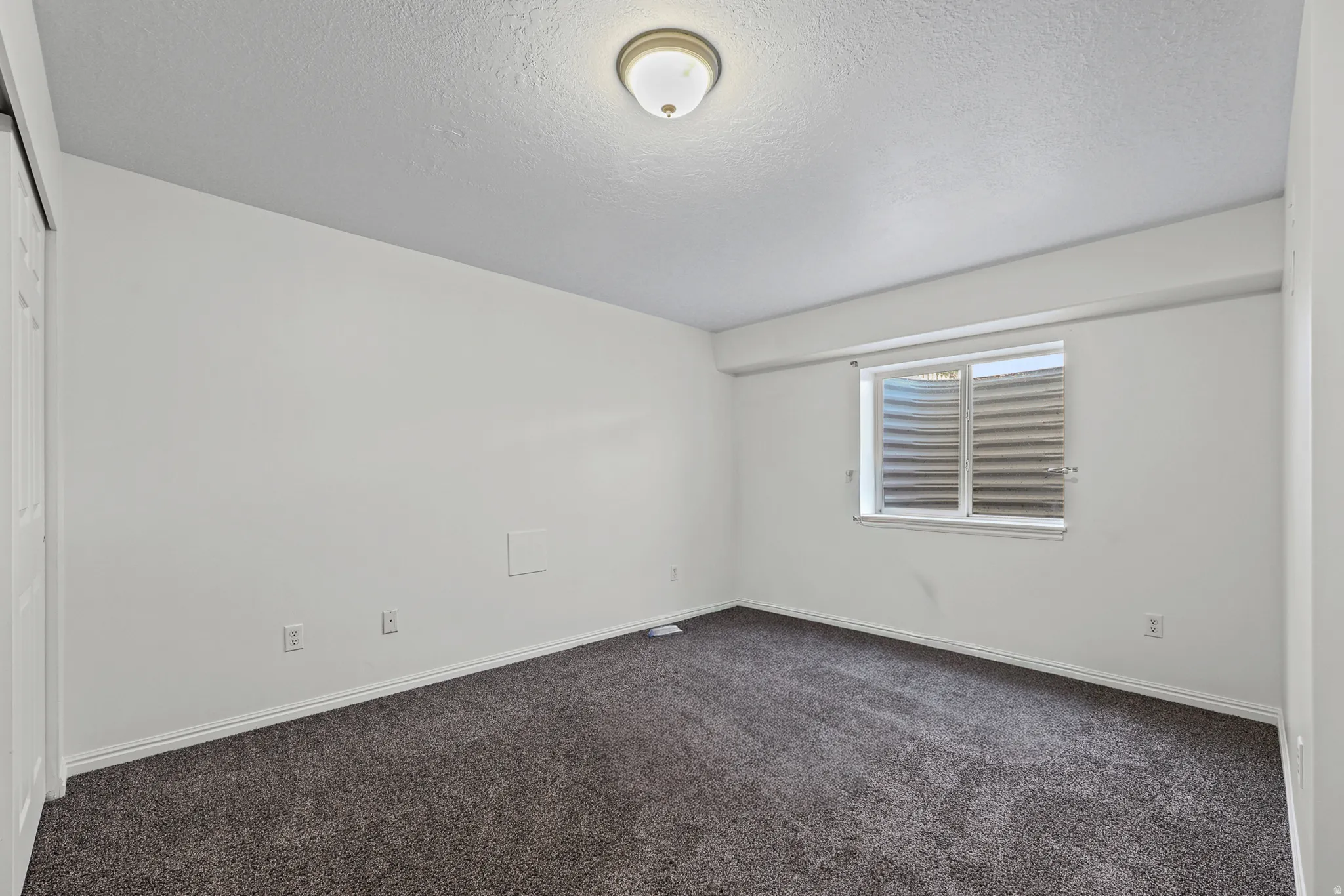 Bedroom featuring a neutral color palette, dark gray carpeting, white baseboards, and a window with a well-cover