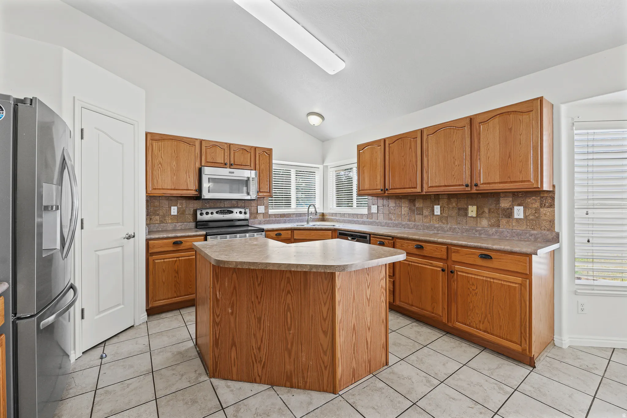 Spacious kitchen featuring an island, extensive wood-finish cabinetry, tile flooring, and vaulted ceilings