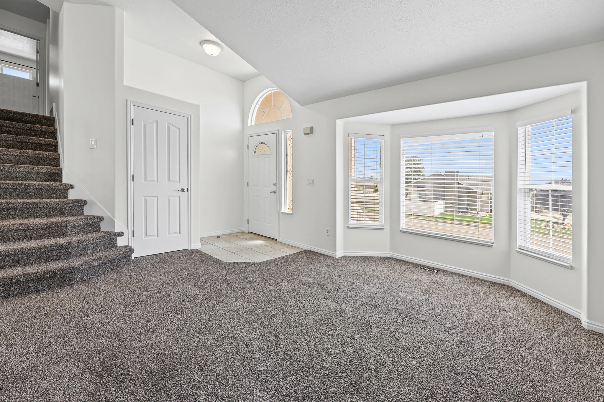 Entryway and living area featuring plush gray carpeting, a bay window with multiple panes, a white paneled door, and a staircase with matching carpeting