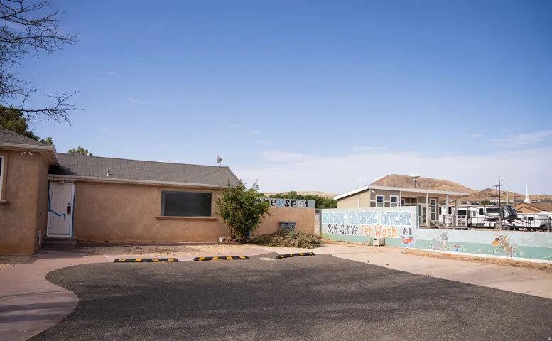 Stucco exterior building with a dark shingle roof and an asphalt parking area