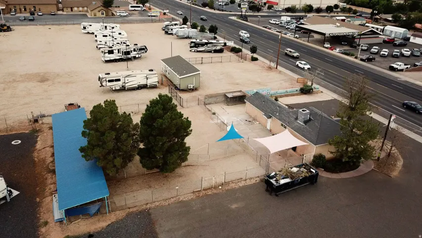 Expansive paved lot with multiple structures, including a single-story building with a dark shingled roof, a blue-canopied shed, and a detached portable structure