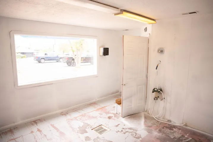 Utility room featuring a wide picture window, fluorescent ceiling lighting, white interior door, wall-mounted faucet, and a floor drain