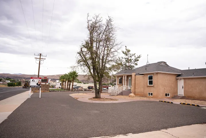 Stucco exterior building featuring a covered entryway with white railings, multiple windows, and an asphalt parking area