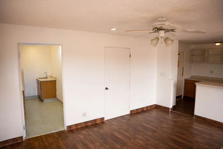 Open concept living area featuring wood-finish flooring, a ceiling fan with integrated lighting, and white baseboards