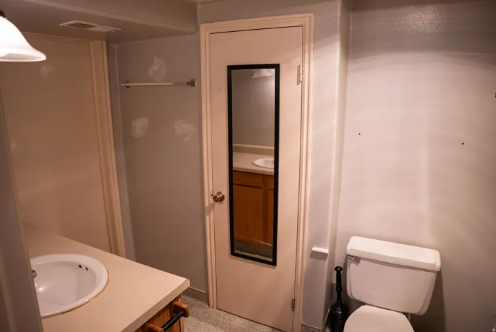 Bathroom featuring a white toilet, light-colored vanity with an integrated sink, and a mirrored door