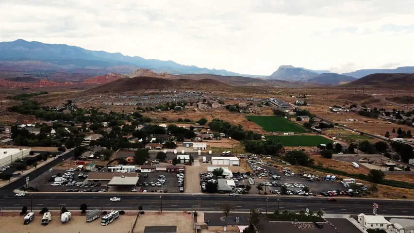 Expansive aerial perspective showcasing a commercial district with a large parking area, highway frontage, and distant mountain ranges