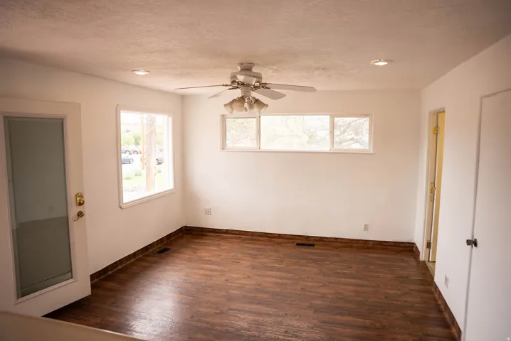 Room featuring wood-finish flooring, white walls, and a ceiling fan with integrated lighting