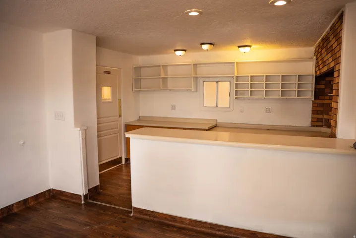 Entertainment space featuring a built-in bar with a light-toned countertop, wood-finish flooring, recessed lighting, and an exposed brick accent wall with an integrated opening