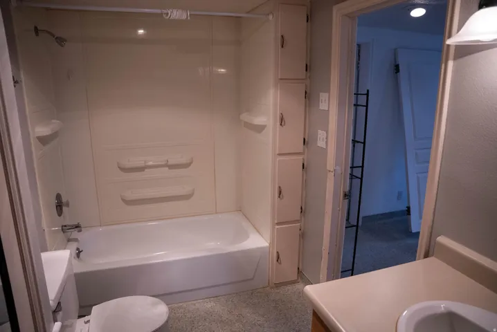 Bathroom featuring a white tub with integrated shower, overhead showerhead, and wall-mounted shelving