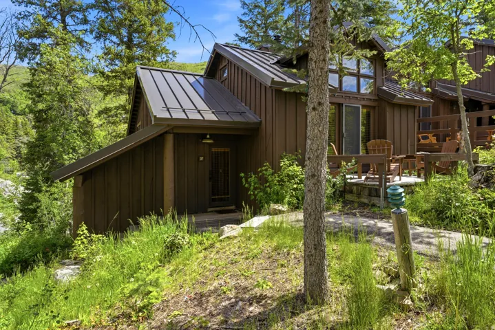 Wood-sided exterior featuring a dark metal roof, multi-pane windows, and an outdoor patio with a privacy railing