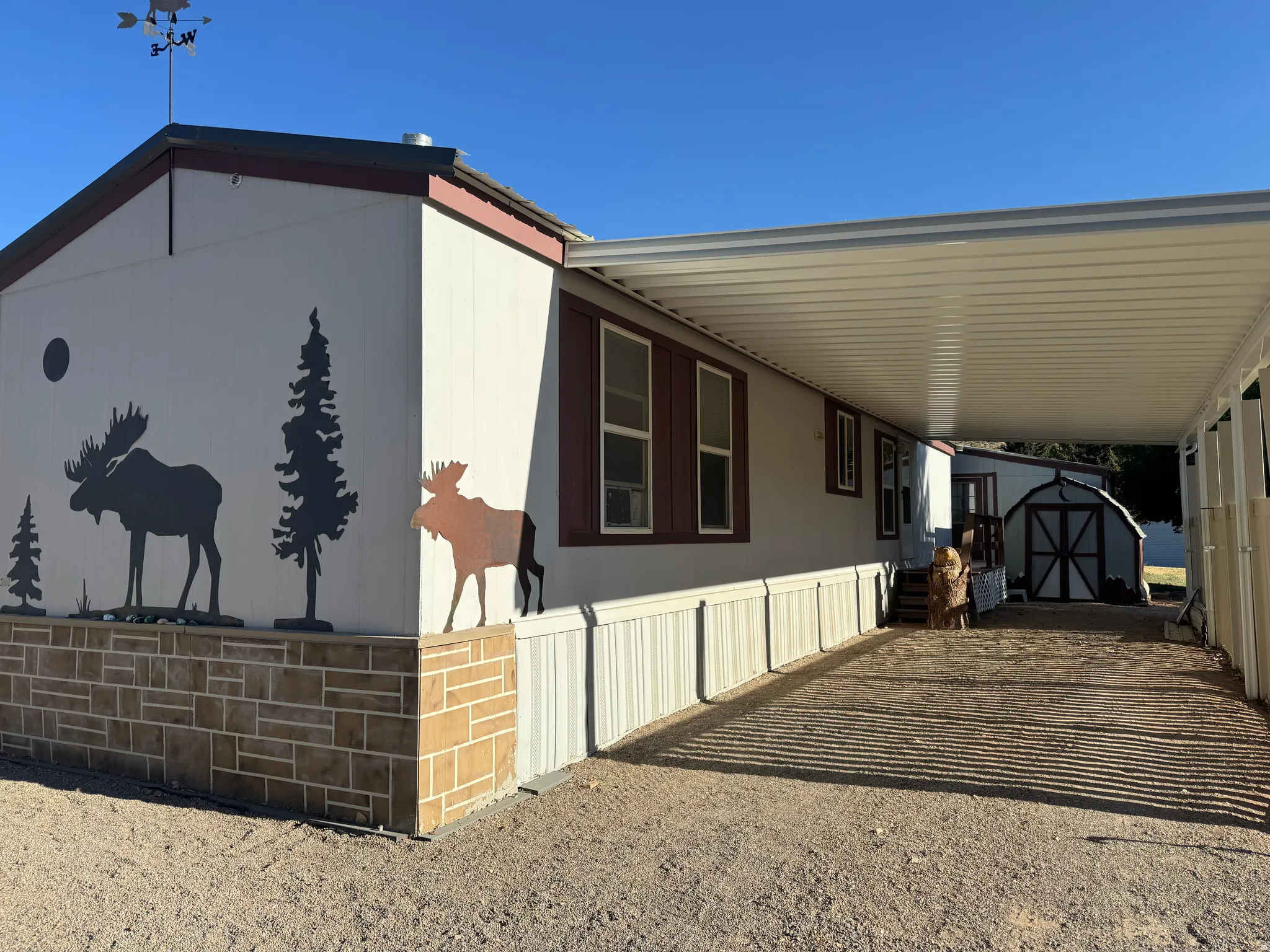 Exterior featuring a carport, decorative stone-look skirting, and a storage shed