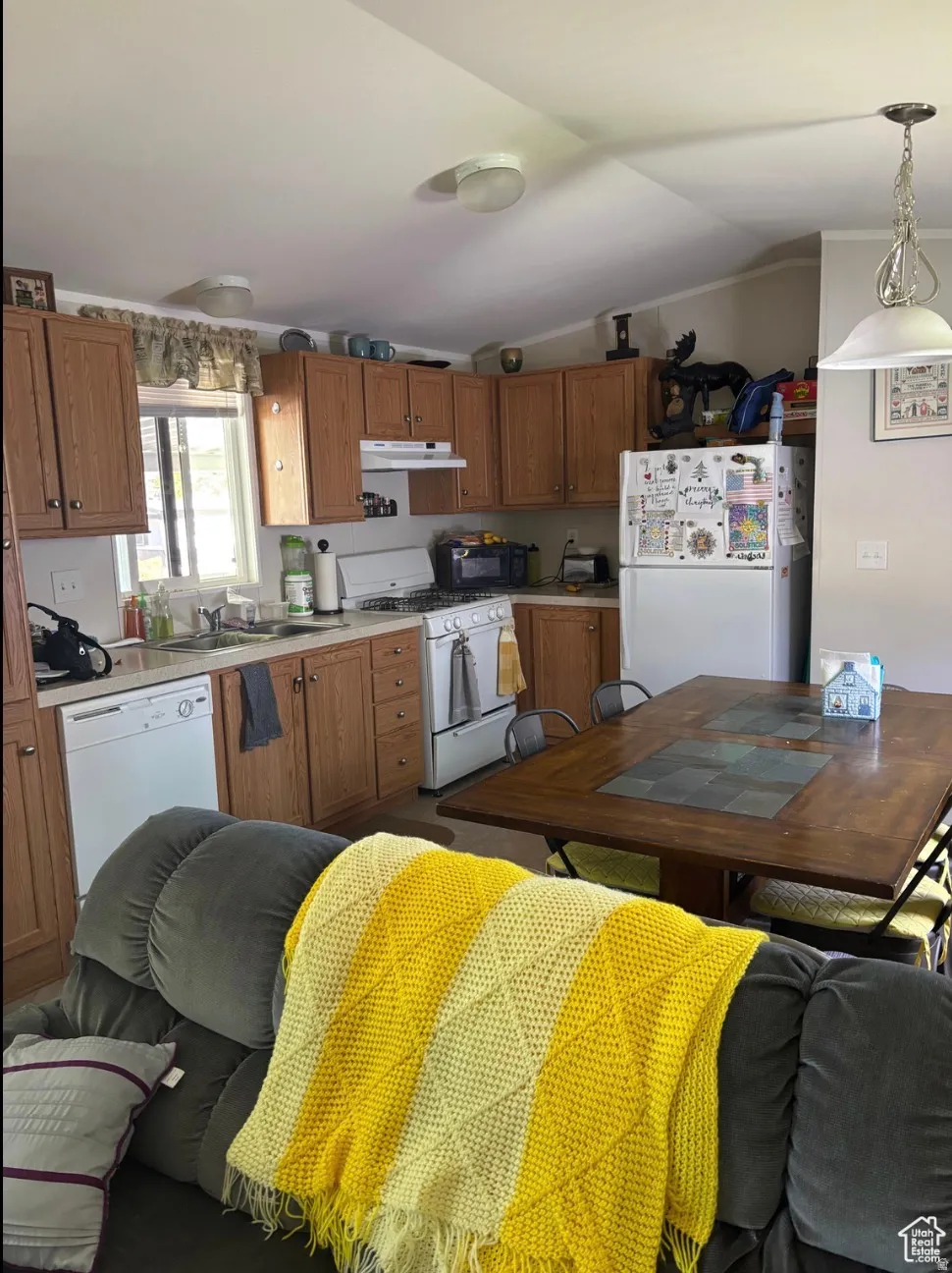 Kitchen area featuring wood-finish cabinetry, white appliances, and a window above the sink