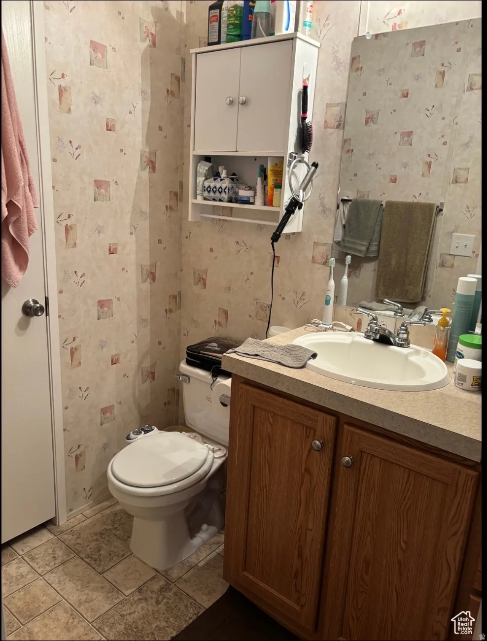 Bathroom featuring a wood-finish vanity with a built-in sink, a wall-mounted medicine cabinet, and patterned wallpaper