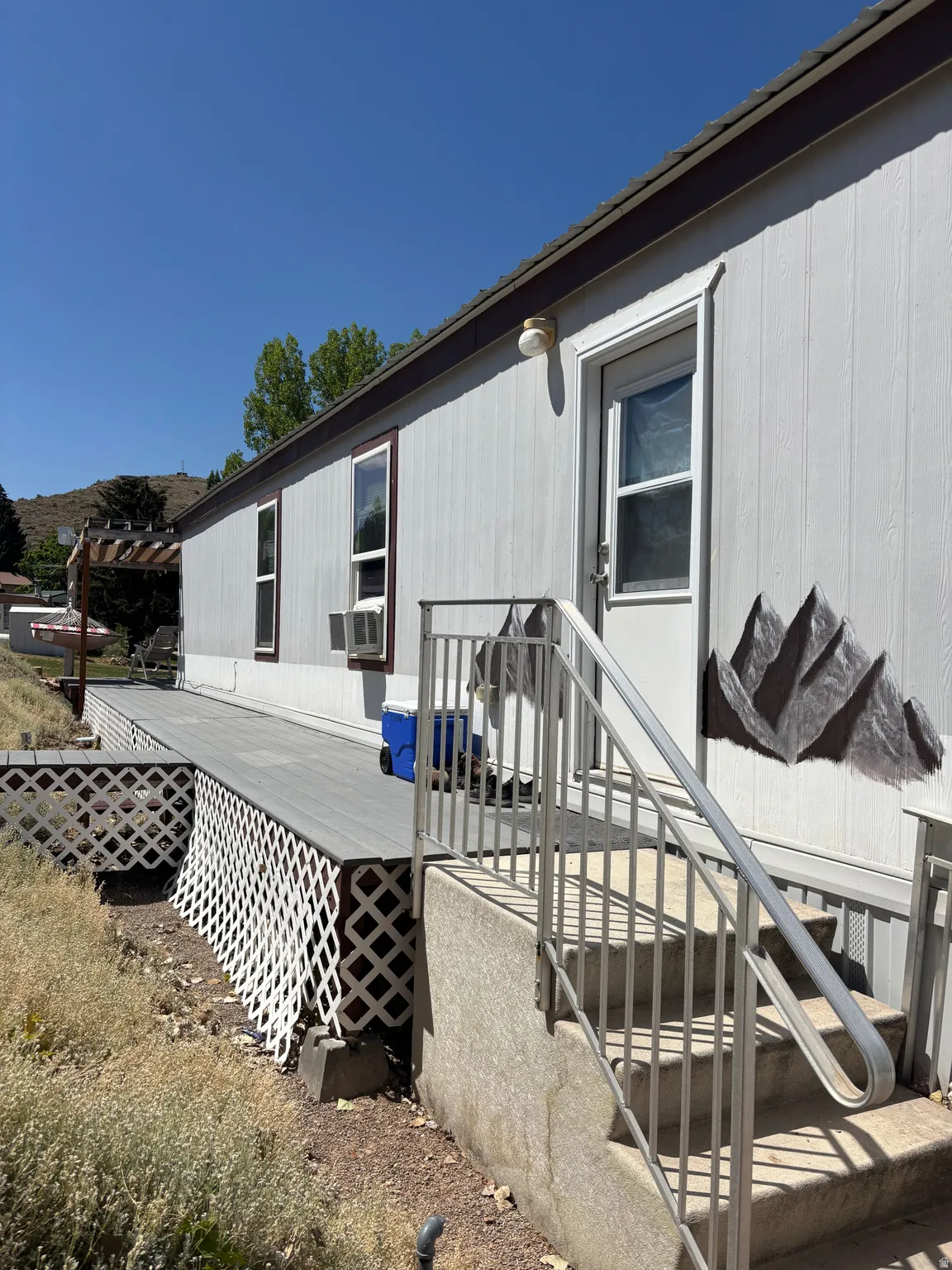 Exterior featuring light-colored siding, a dark roofline, and a deck with lattice skirting
