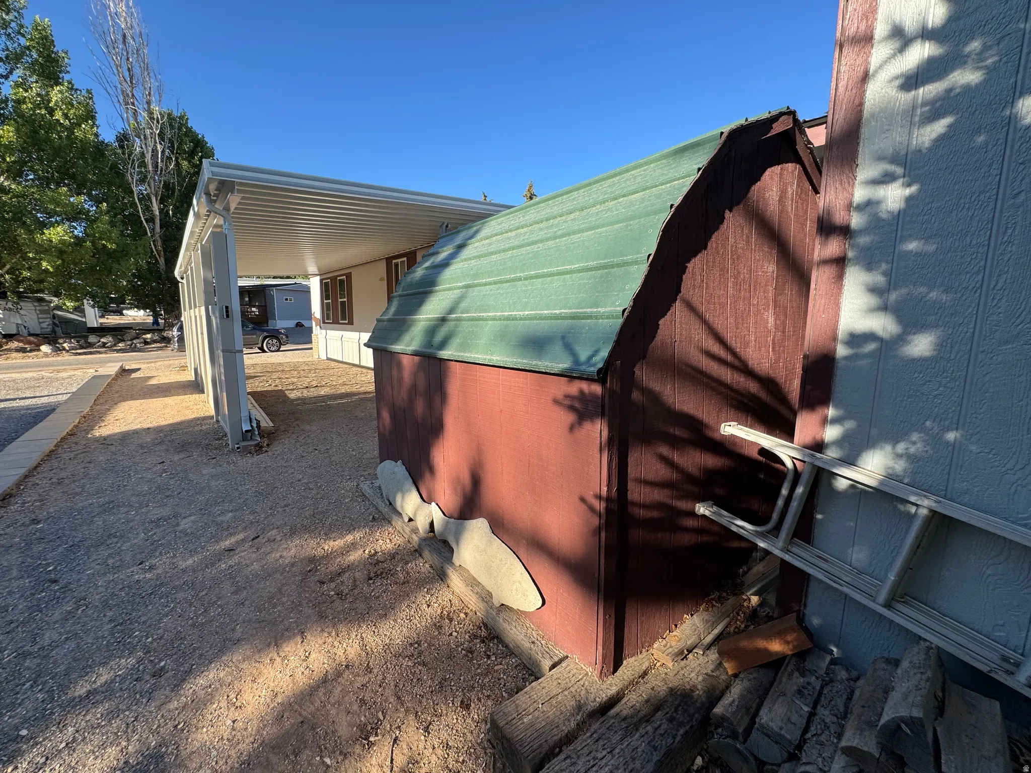 Freestanding shed with a green metal roof and red wood-finish siding, positioned on a gravel lot