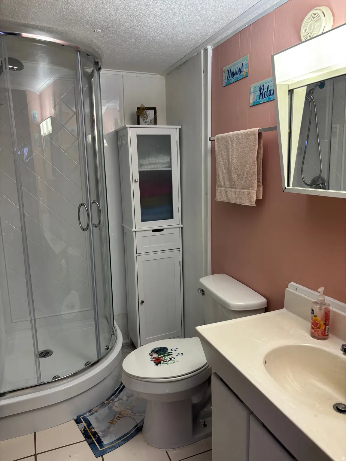 Corner shower enclosure with glass doors, white vanity with integrated sink, paneling, and white tile flooring