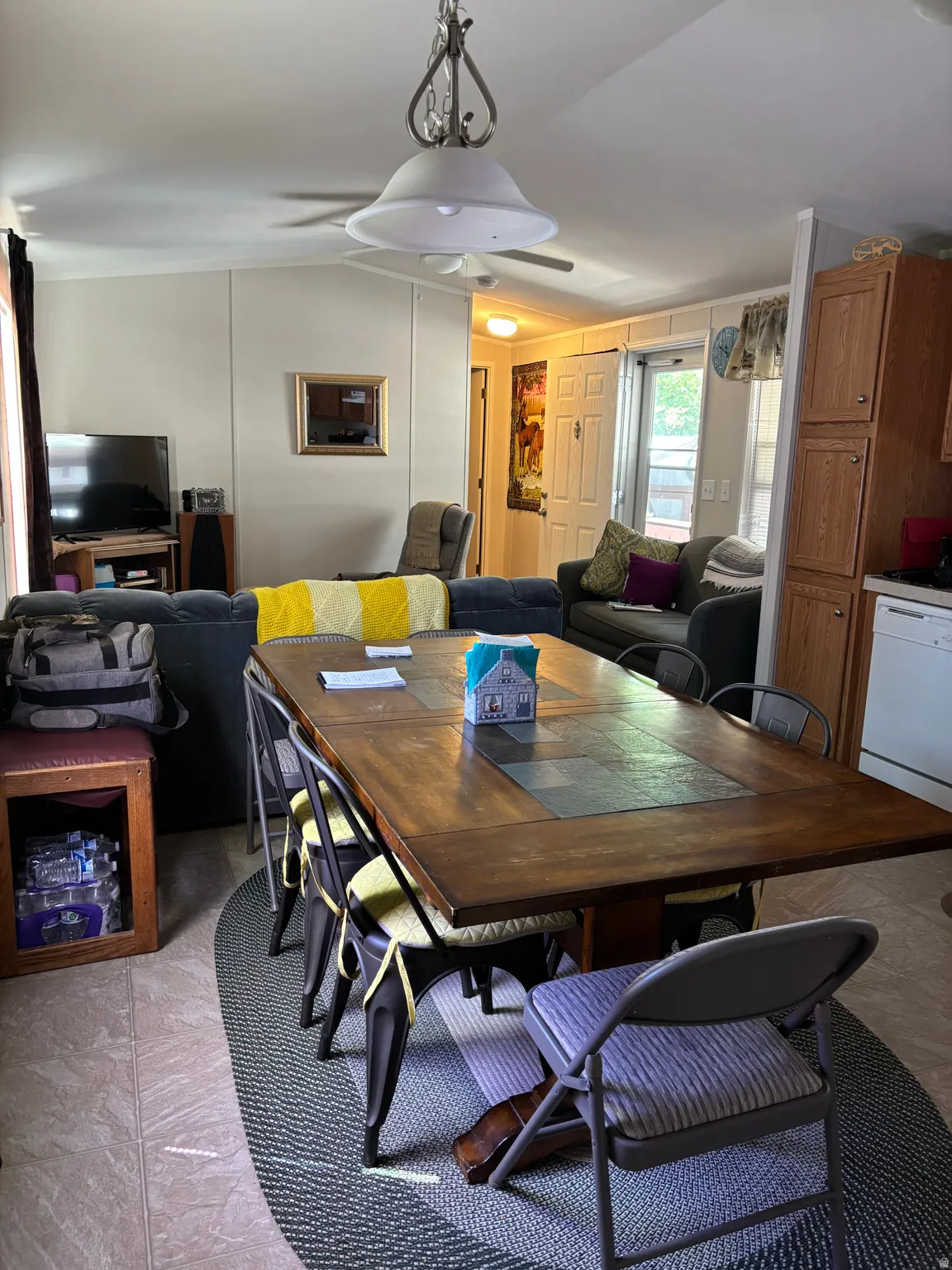Dining area featuring a wood-finish table with stone-inlay accents, tile flooring, and a ceiling-mounted light fixture with a fan