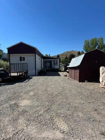 Gravel driveway leading to a residence with white siding and a dark roof