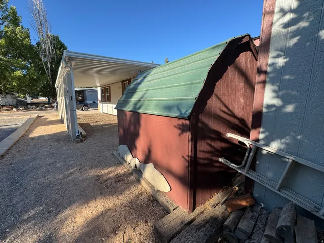 Freestanding shed with a green metal roof and red wood-finish siding, positioned on a gravel lot