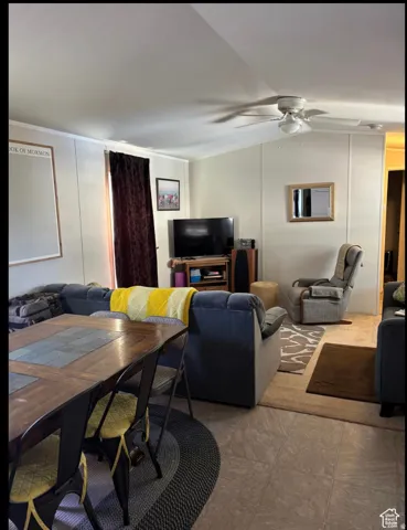 Open-concept living space featuring neutral tone flooring, a ceiling fan with integrated lighting, and vertical wall paneling