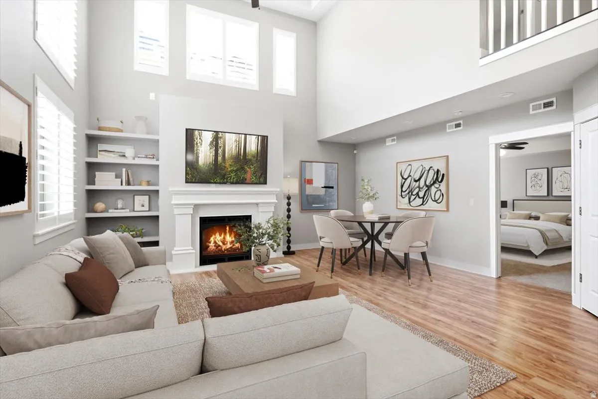 Vaulted living room featuring a decorative fireplace with a mantel, built-in shelving, hardwood-finish flooring, and white plantation shutters