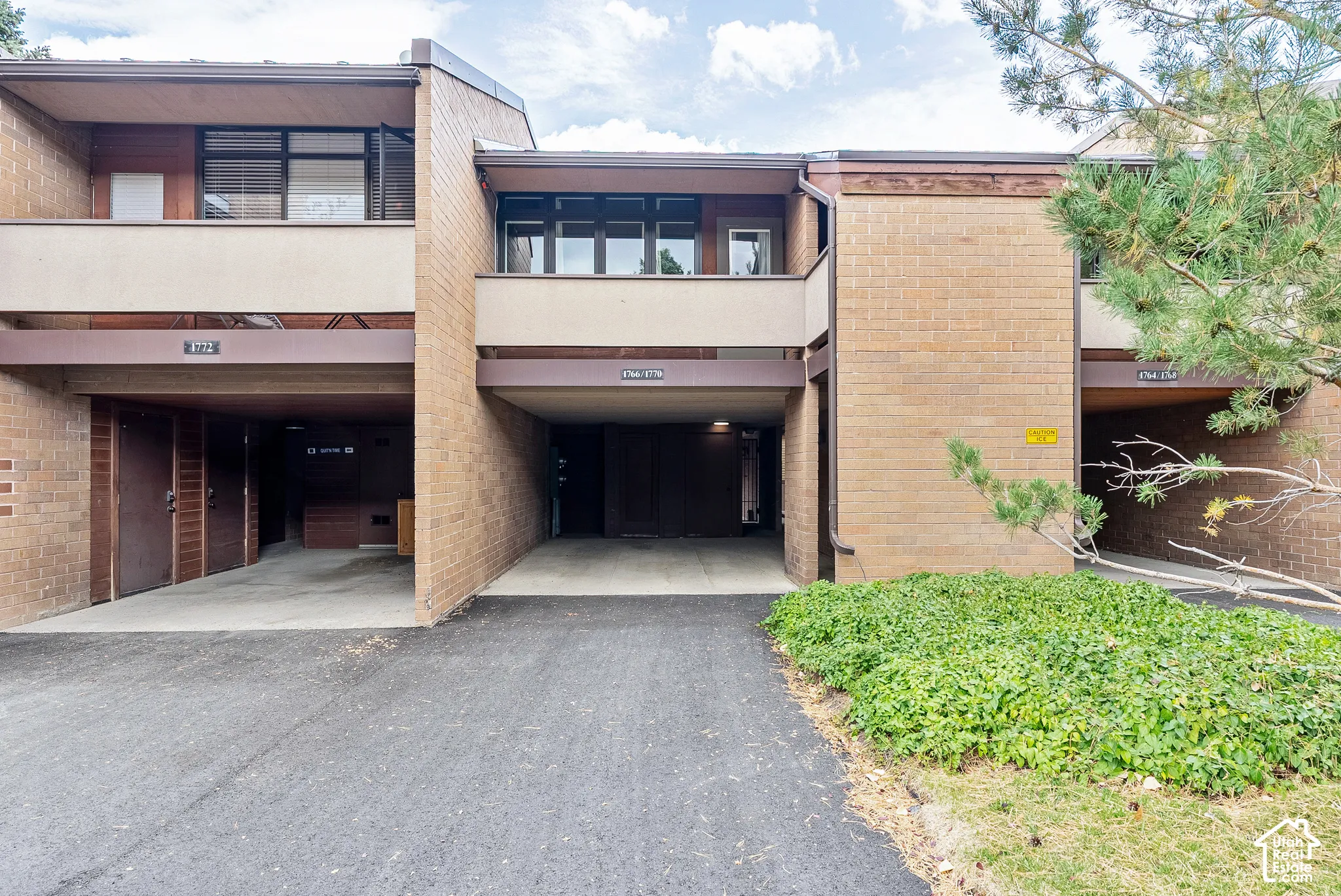 Multi-level brick exterior featuring covered parking, second-story balconies with dark window frames, and mature landscaping