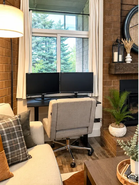 Exposed brick wall, floor-to-ceiling brick fireplace surround, wood-finish flooring, and large sliding window with exterior tree-lined backdrop