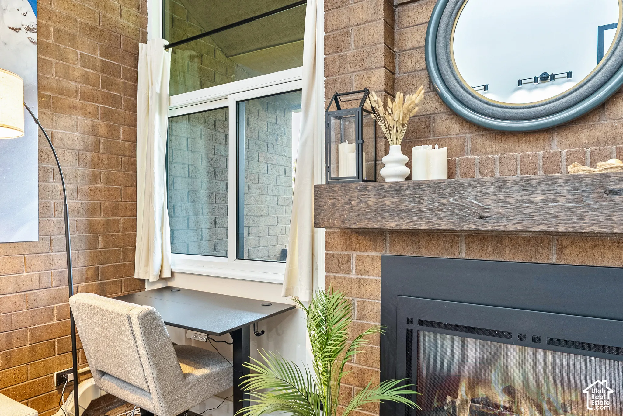 Exposed brick wall with an integrated fireplace featuring a substantial wood mantel