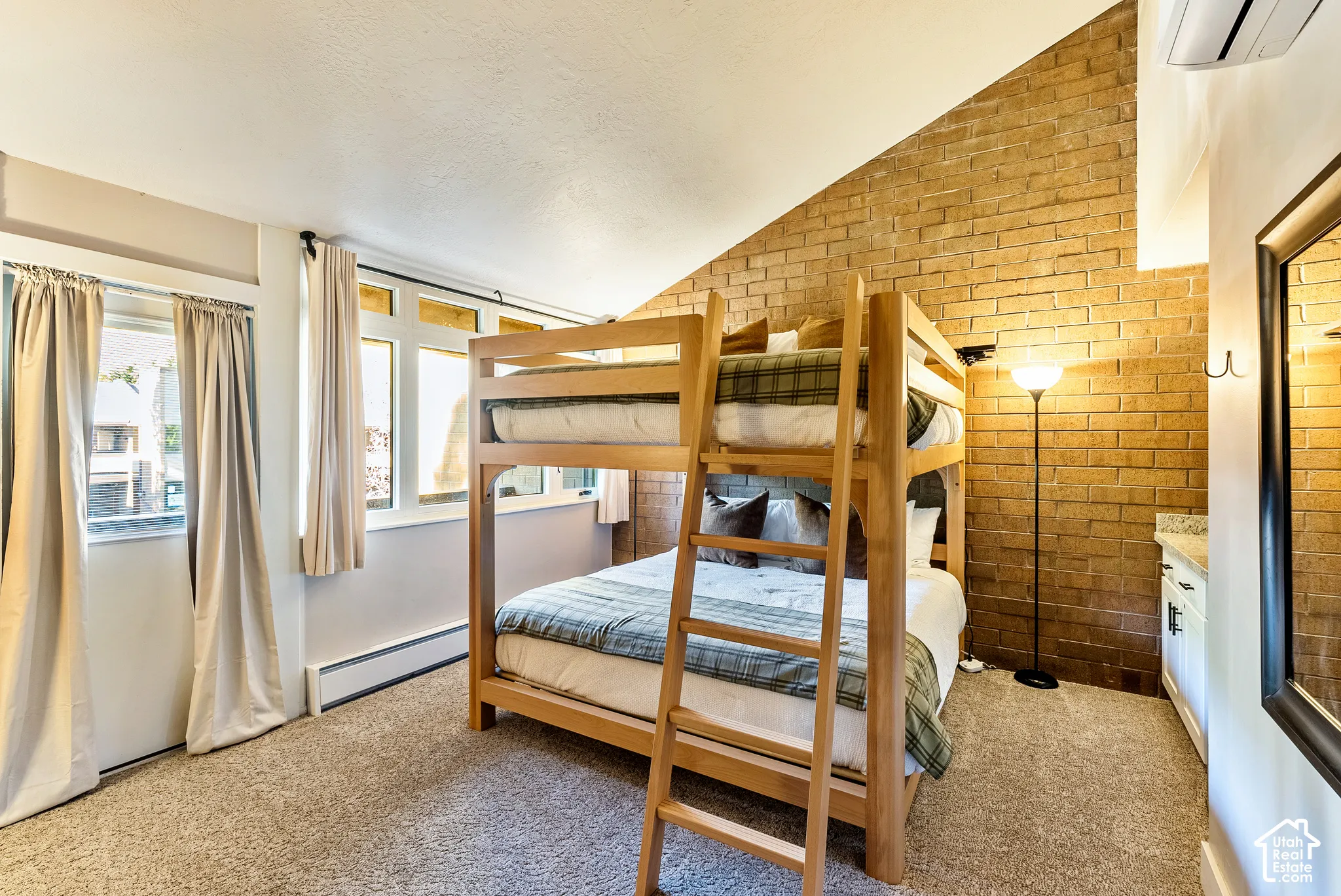 Angled brick accent wall with bunk beds, carpeted flooring, and multiple windows