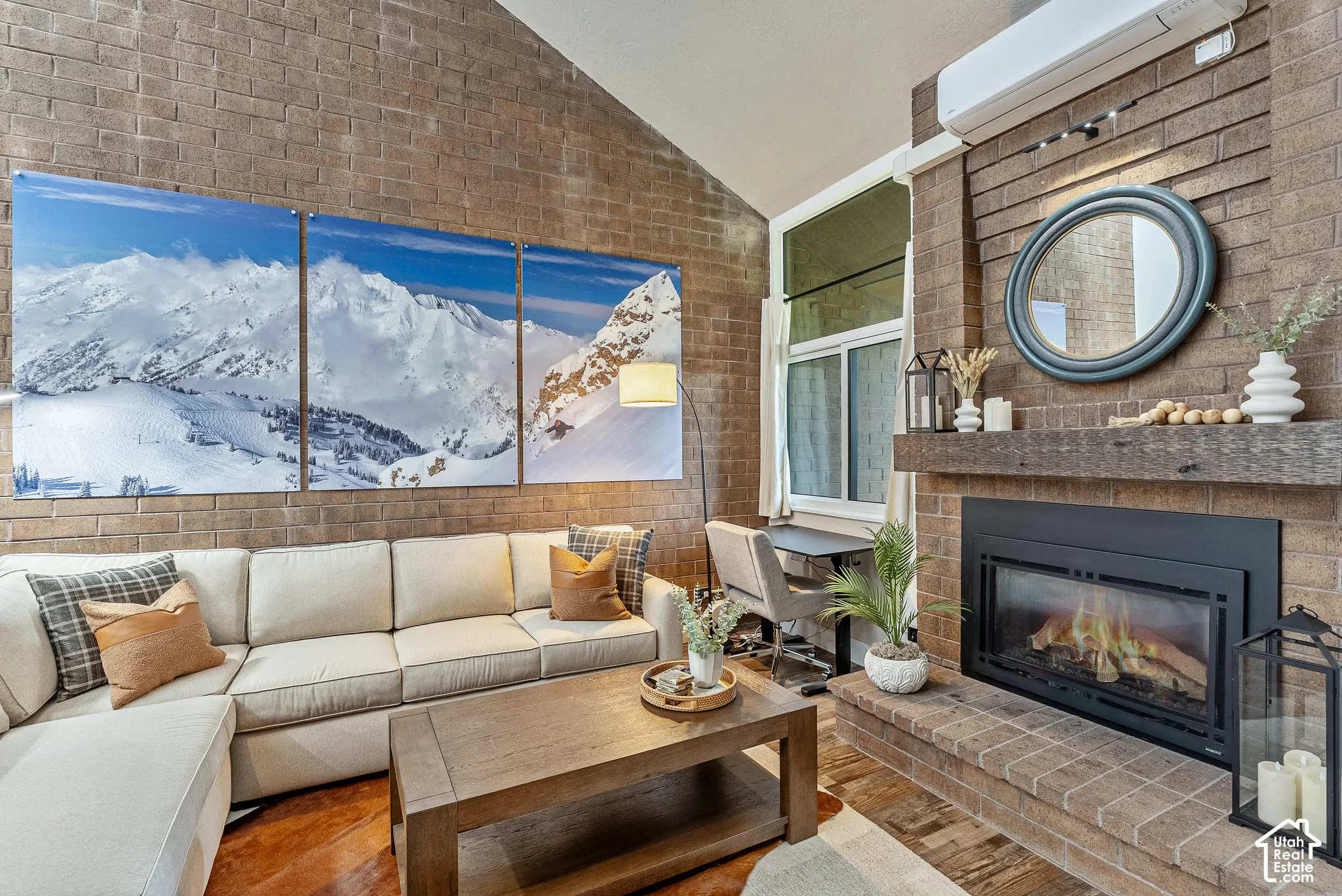 Living area featuring a floor-to-ceiling brick accent wall, vaulted ceiling, and a built-in fireplace with a substantial wood mantel