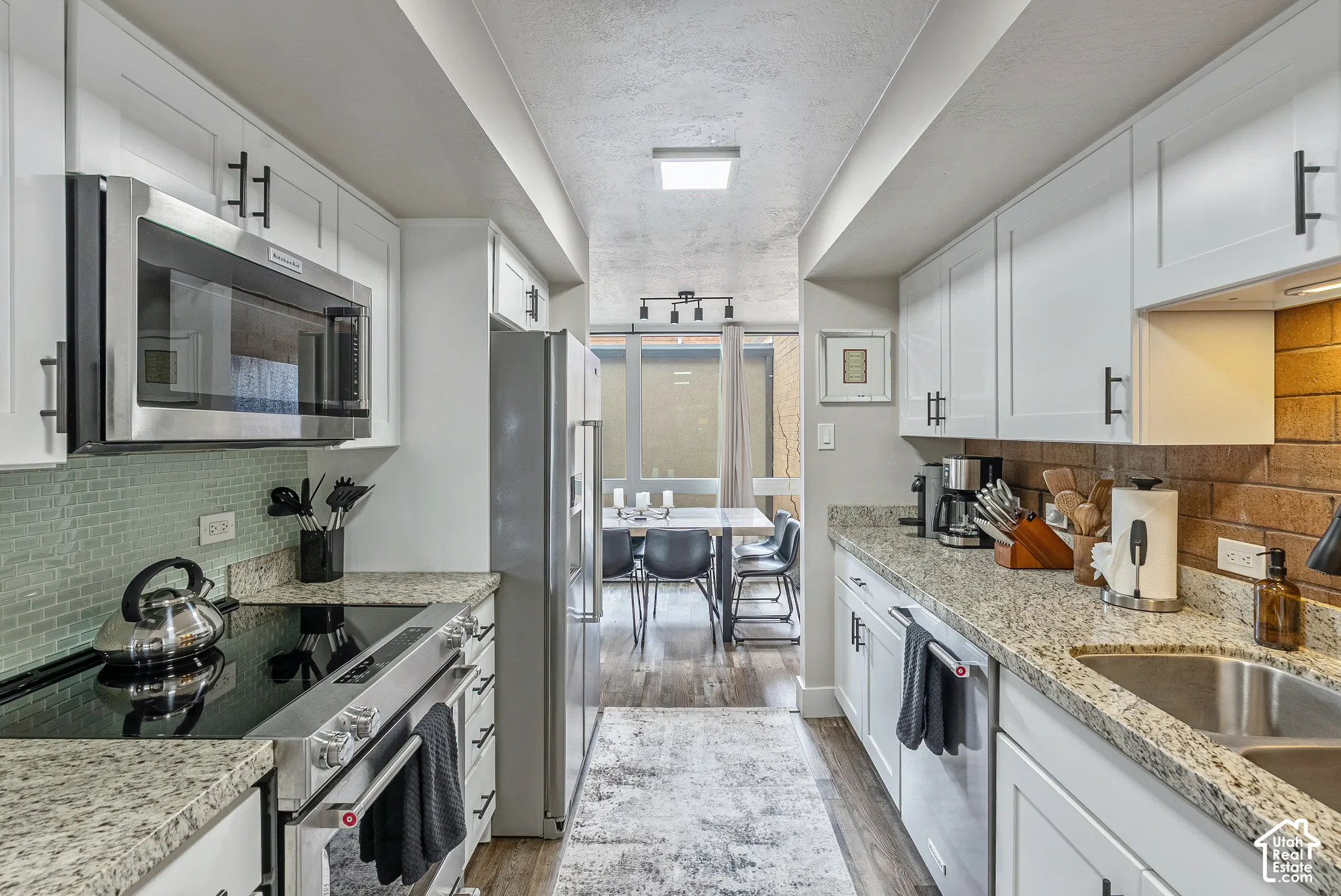 Galley kitchen featuring white shaker cabinetry with black hardware, stainless steel appliances including an over-the-range microwave and electric range, and granite countertops