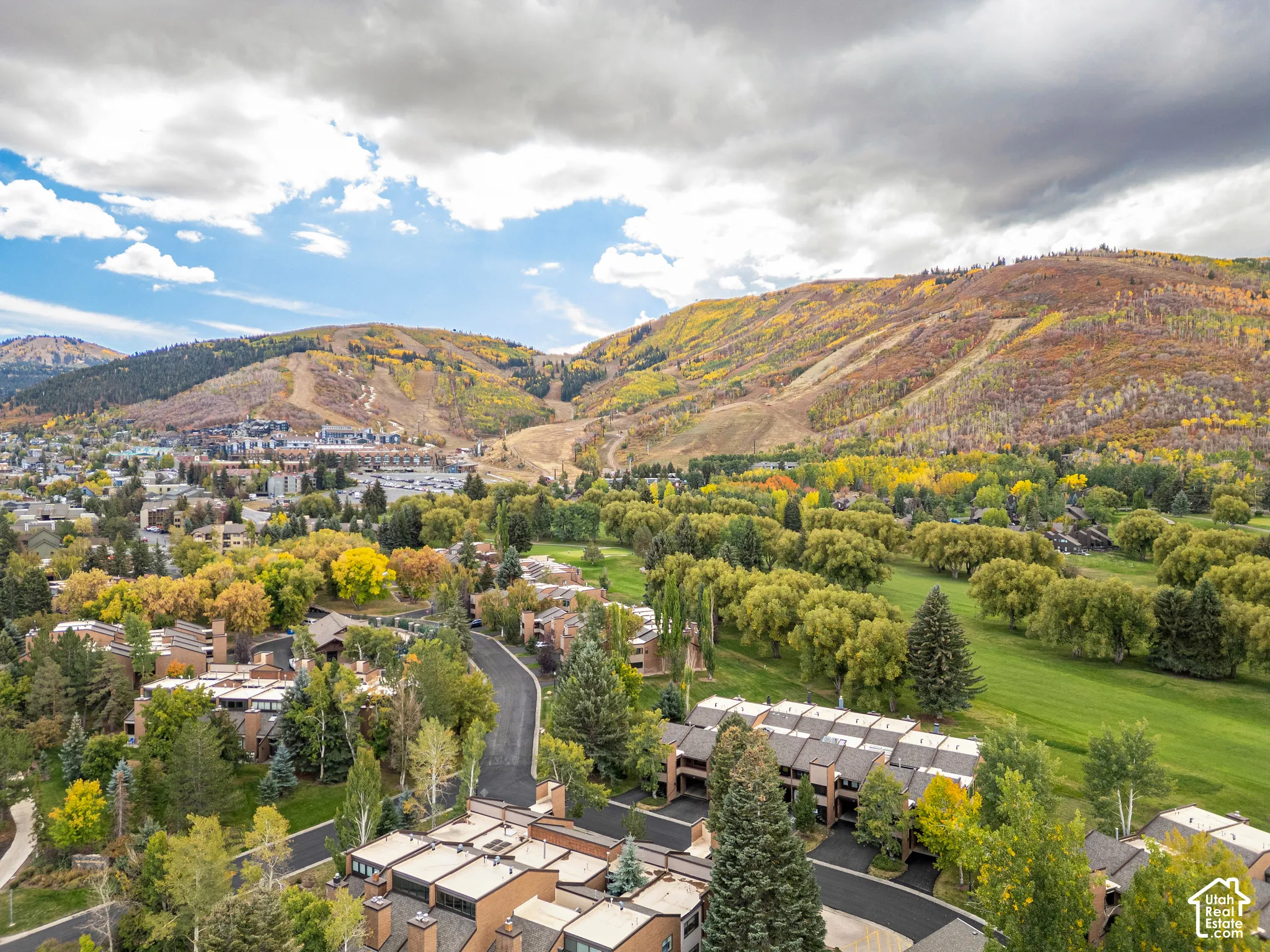 Aerial landscape featuring residential properties set against a backdrop of mountainous terrain with autumnal foliage and a green golf course