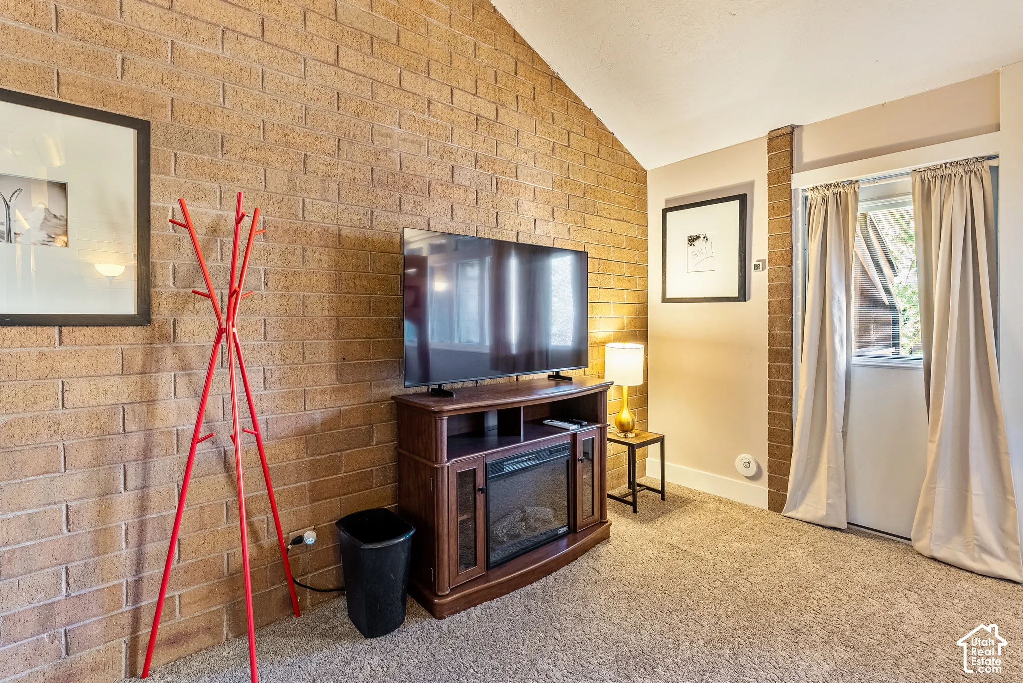 Exposed brick wall with vaulted ceiling and plush carpet flooring
