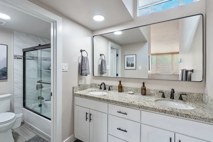 Bathroom featuring a dual vanity with light granite countertops, white cabinetry, and matte black hardware