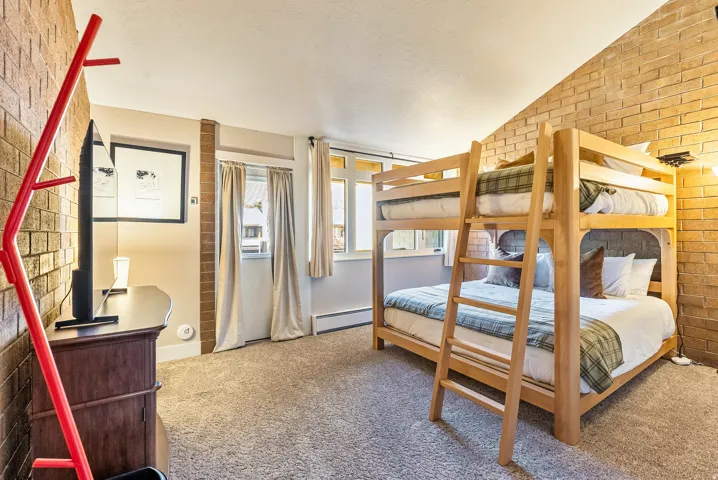 Accommodating room featuring a wooden bunk bed, light brown brick accent walls, and neutral-toned carpeting