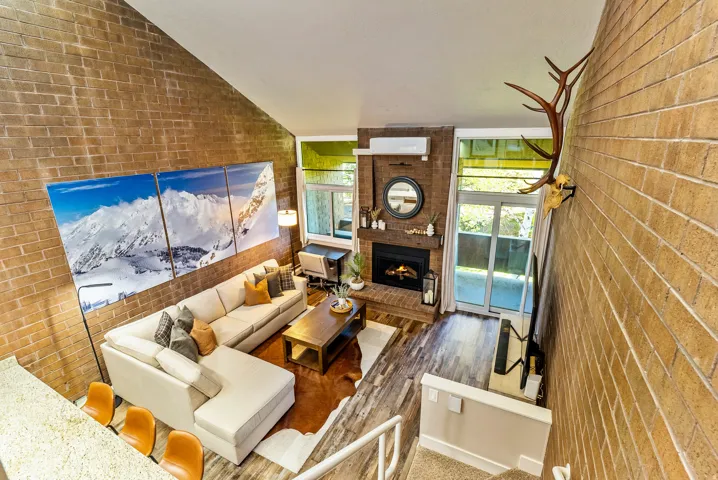 Great room featuring vaulted ceilings, a brick accent wall, wood-finish flooring, and a fireplace with a wood mantle
