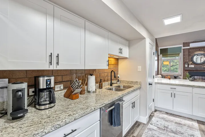 Contemporary kitchen featuring white cabinetry with matte black hardware, granite-style countertops, a brick-patterned backsplash, and a double basin stainless steel sink with a matte black faucet