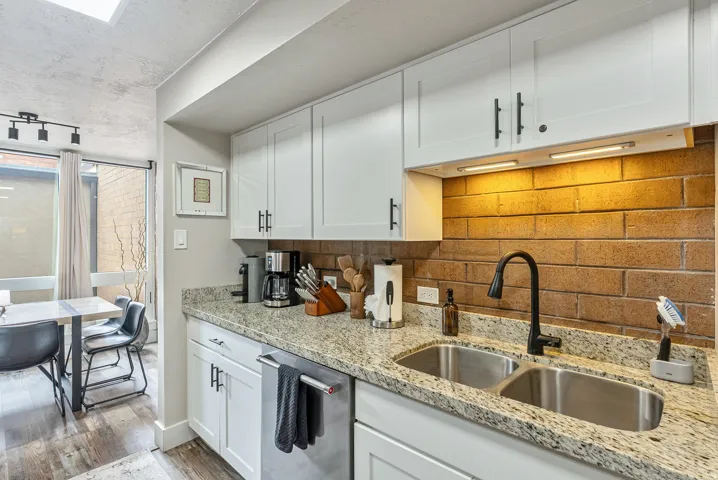Kitchen featuring white shaker cabinetry, granite-finish countertops, and a brick-finish backsplash
