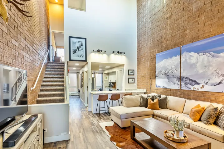 Living area featuring a soaring ceiling, exposed brick accent wall, wood-finish flooring, and a breakfast bar with stone-look countertop