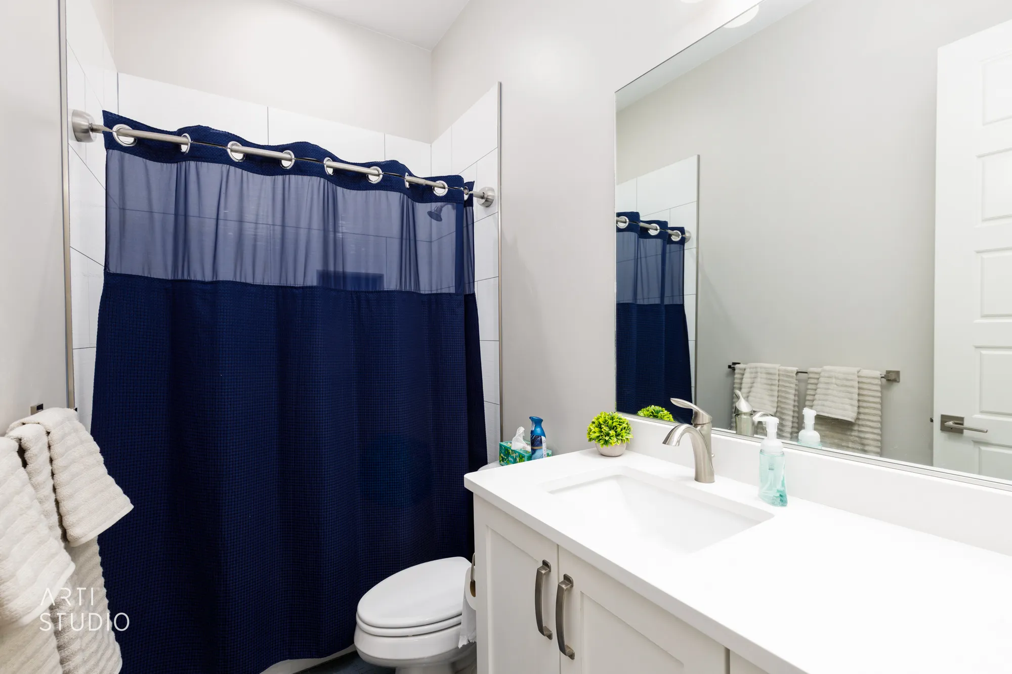 Modern bathroom featuring a white vanity with integrated sink, brushed nickel faucet, large wall mirror, and white tiled shower surround