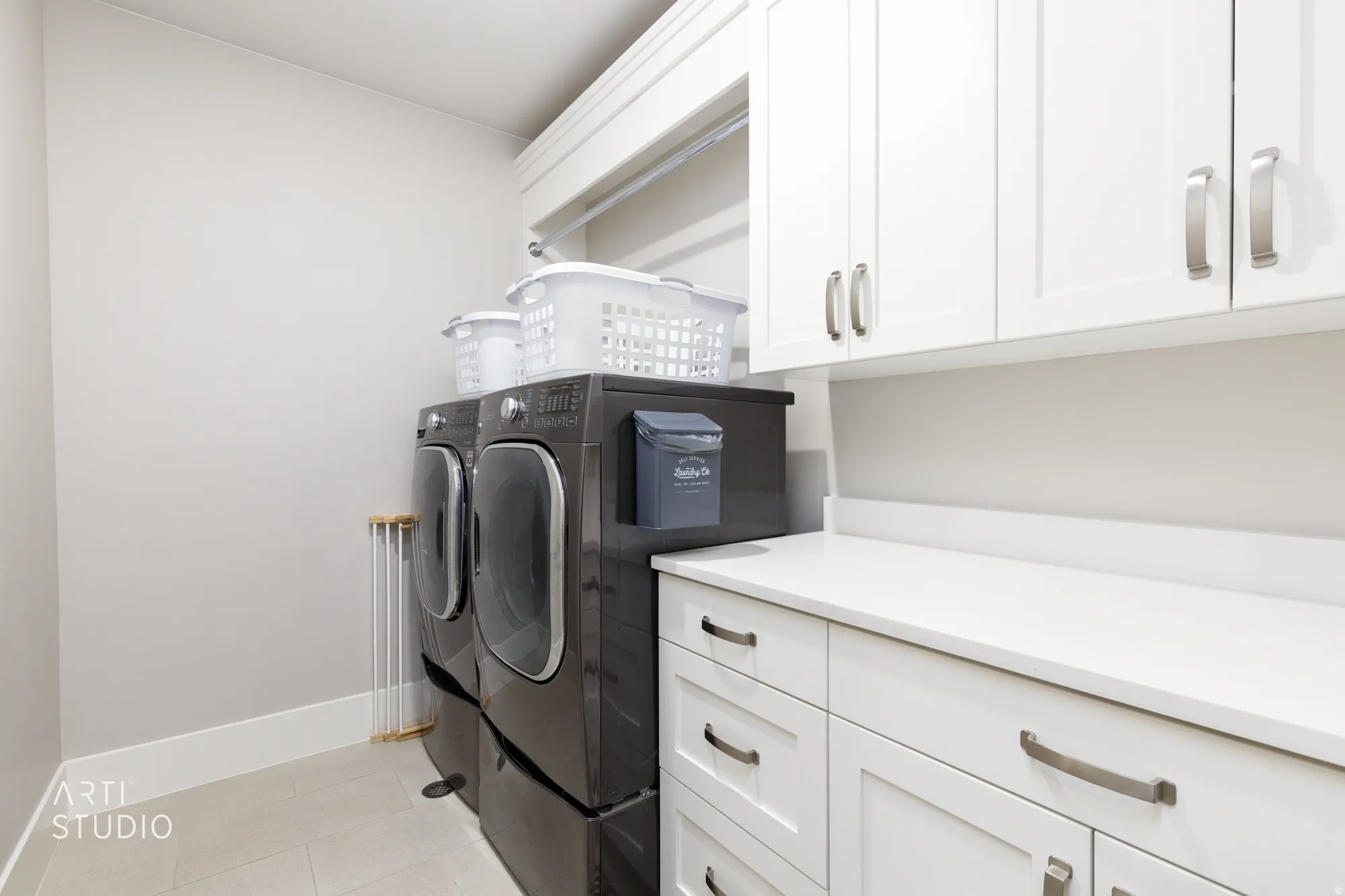 Laundry area featuring white shaker-style cabinetry with brushed nickel hardware, a white countertop, and light-toned tile flooring