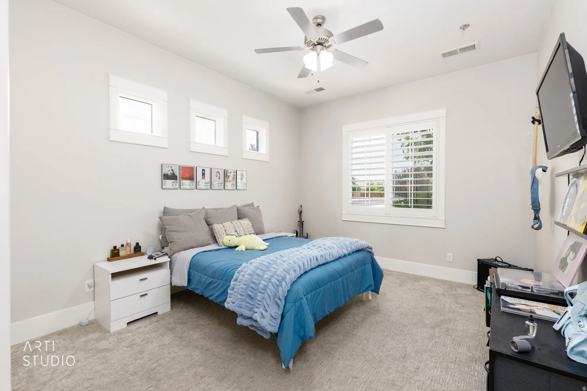 Carpeted room featuring a ceiling fan with integrated lighting, a large window with white louvered shutters, and three transom windows