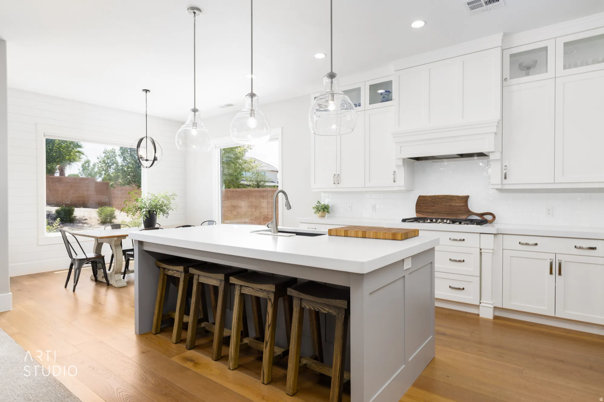 Spacious kitchen featuring a large central island with seating, pendant lighting, white shaker cabinetry, and wood-finish flooring