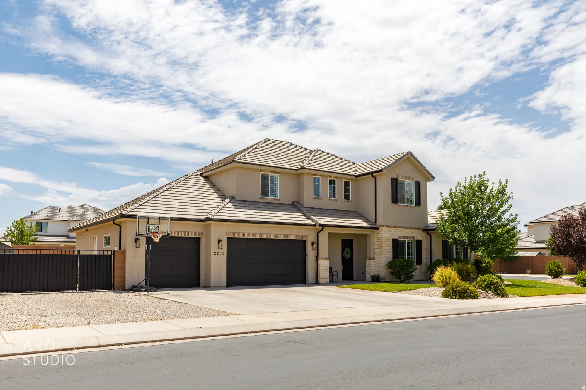 Two-story stucco exterior with stone accents, a tile roof, an attached three-car garage, and a landscaped front yard with mature trees