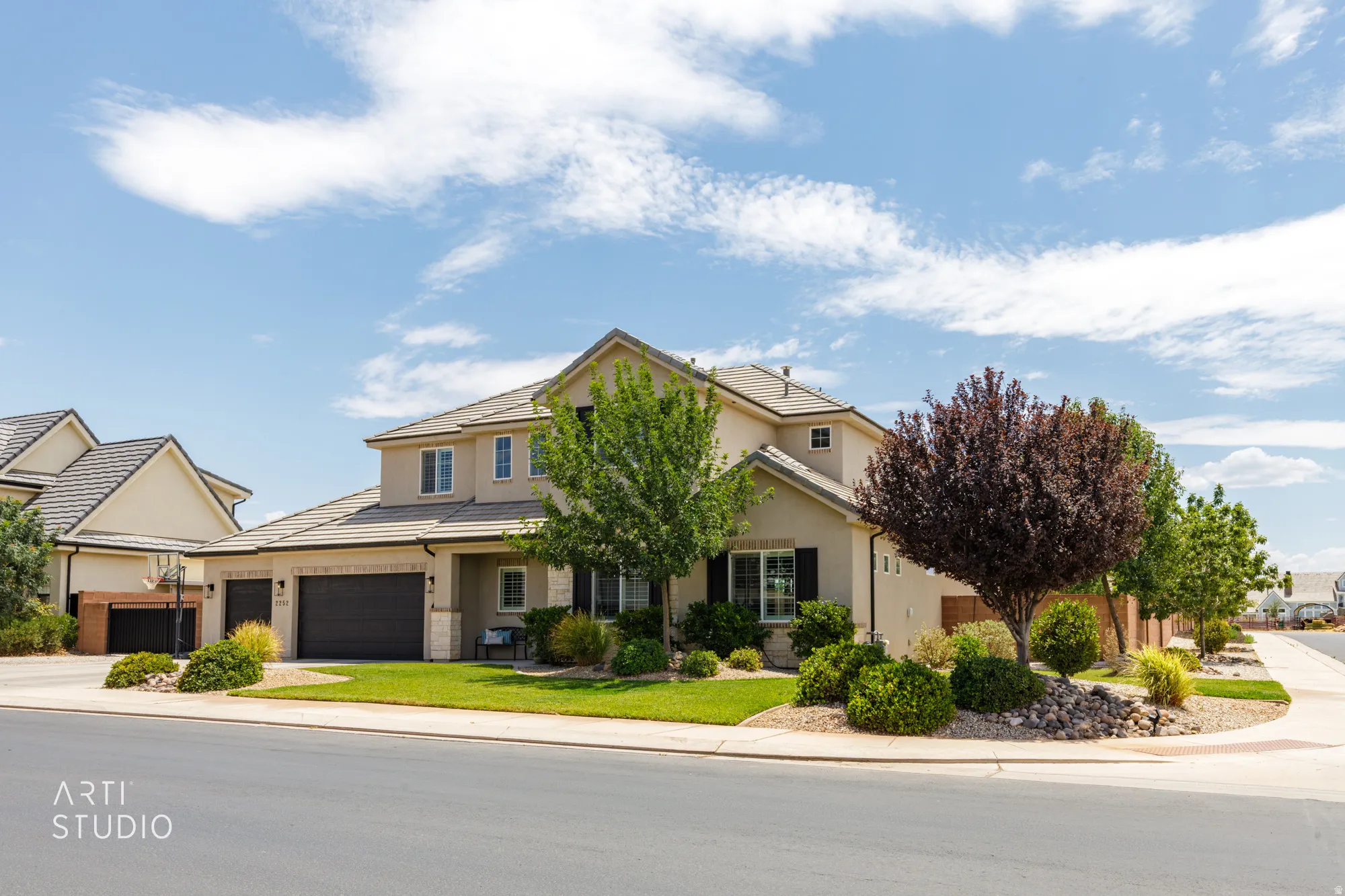 Stucco exterior residence featuring a two-car garage, mature landscaping, and a tiled roof